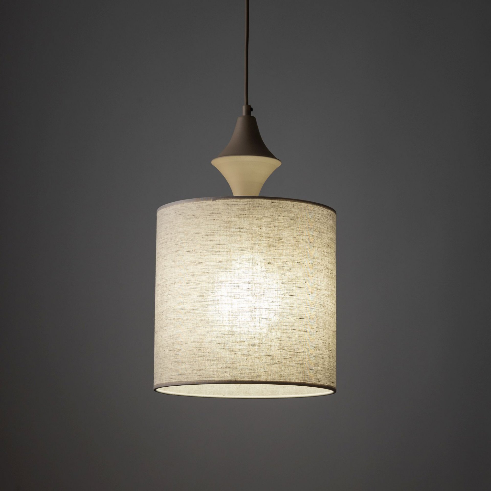 Na obrazie widoczna jest wisząca lampa z beżowym, lnianym abażurem. Lampa jest włączona, emitując ciepłe światło.