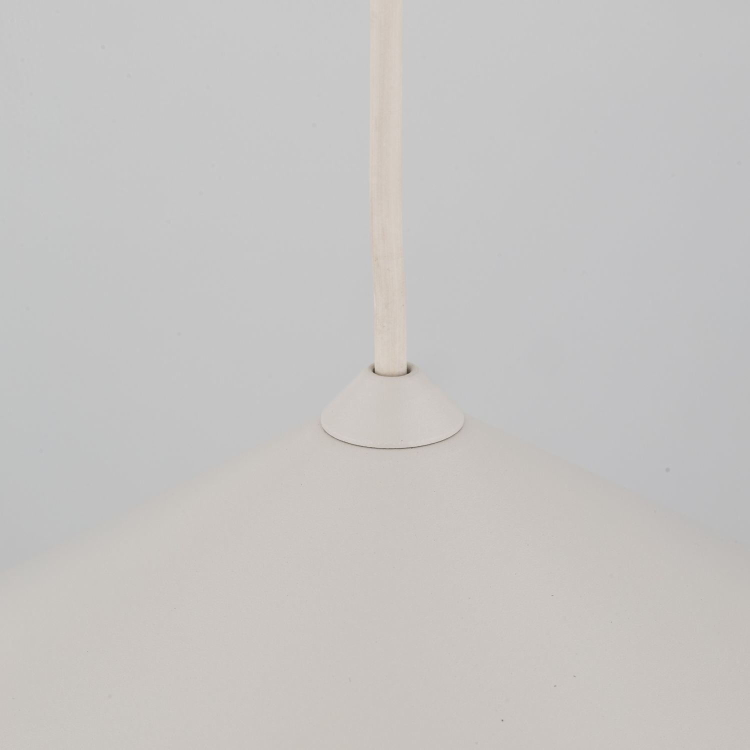 Obraz przedstawia górną część beżowej lampy wiszącej z przewodem wychodzącym z jej środka. Lampa ma gładką powierzchnię i stożkowaty kształt.