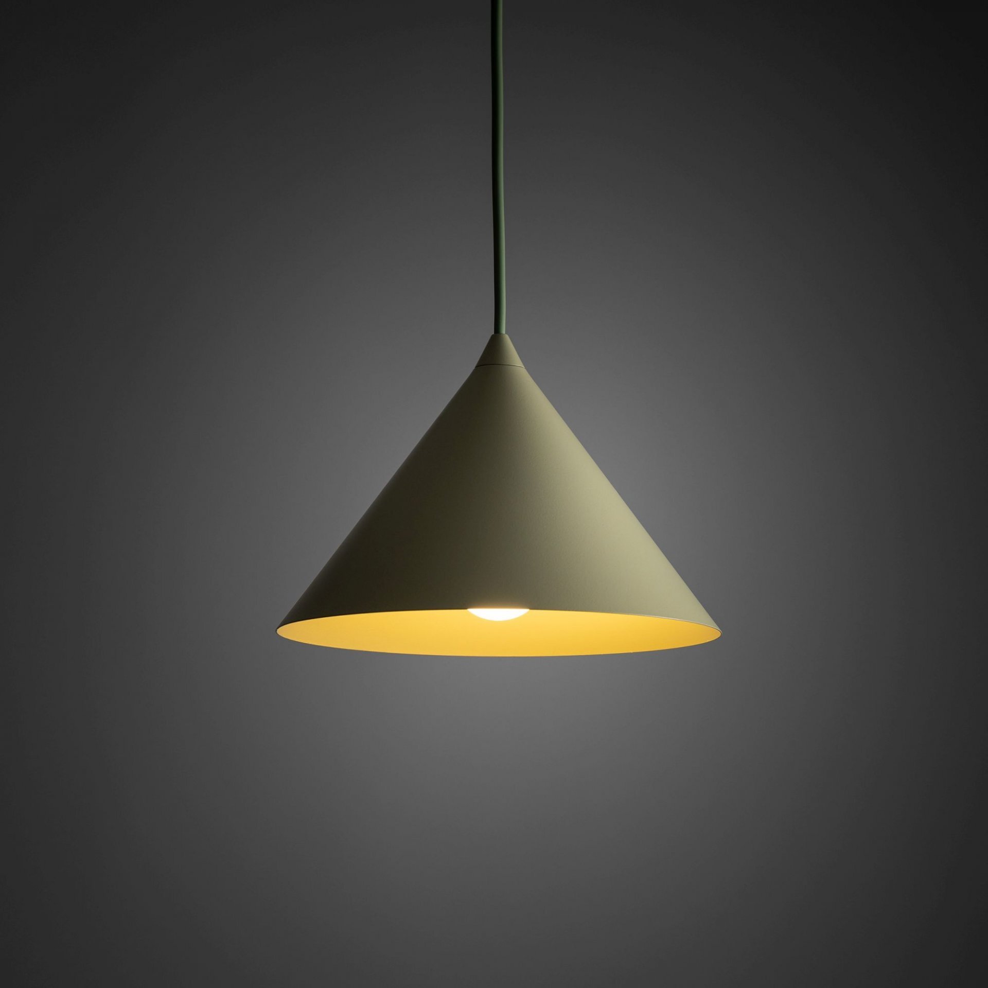 Lampa wisząca w kształcie stożka w kolorze pistacjowym, z widocznym źródłem światła u dołu. Tło jest ciemne, co podkreśla jasność lampy.