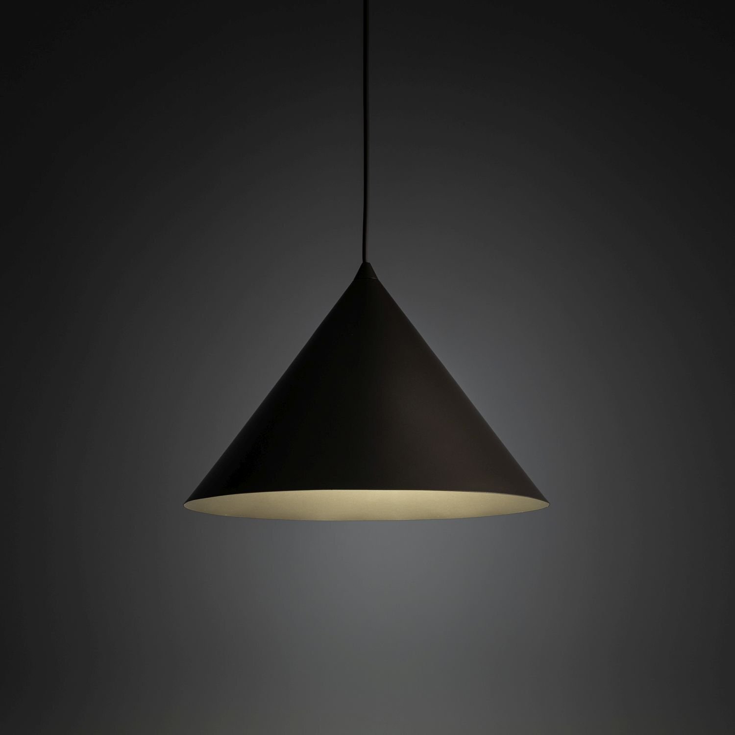 Na obrazie widoczna jest wisząca lampa w kształcie stożka, wykonana z ciemnego materiału. Lampa emituje delikatne światło, a jej przewód jest cienki i czarny.