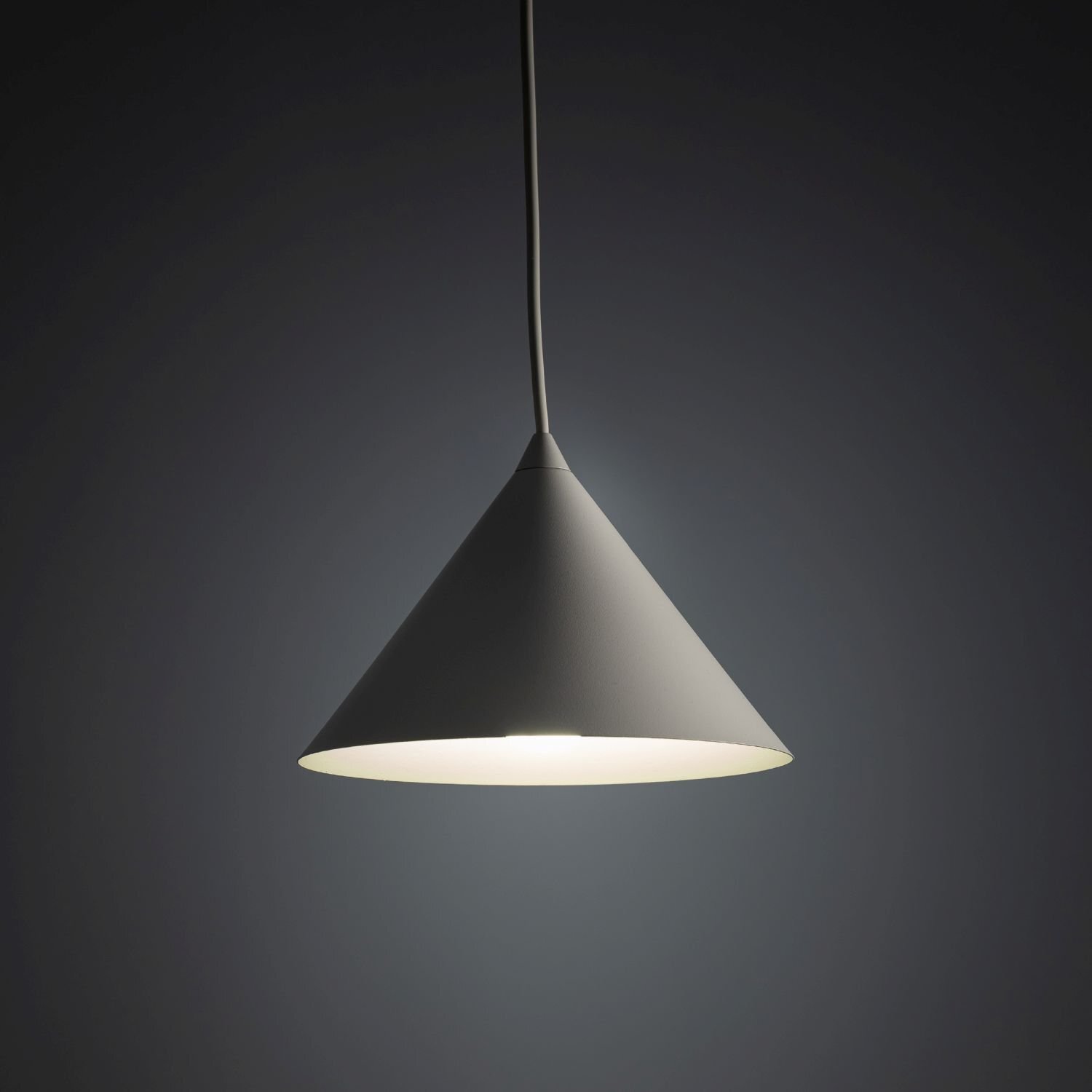Na obrazie widoczna jest lampa wisząca o stożkowym kształcie, emitująca światło w dół. Lampa jest zawieszona na cienkim przewodzie, a jej powierzchnia jest gładka i jednolita.