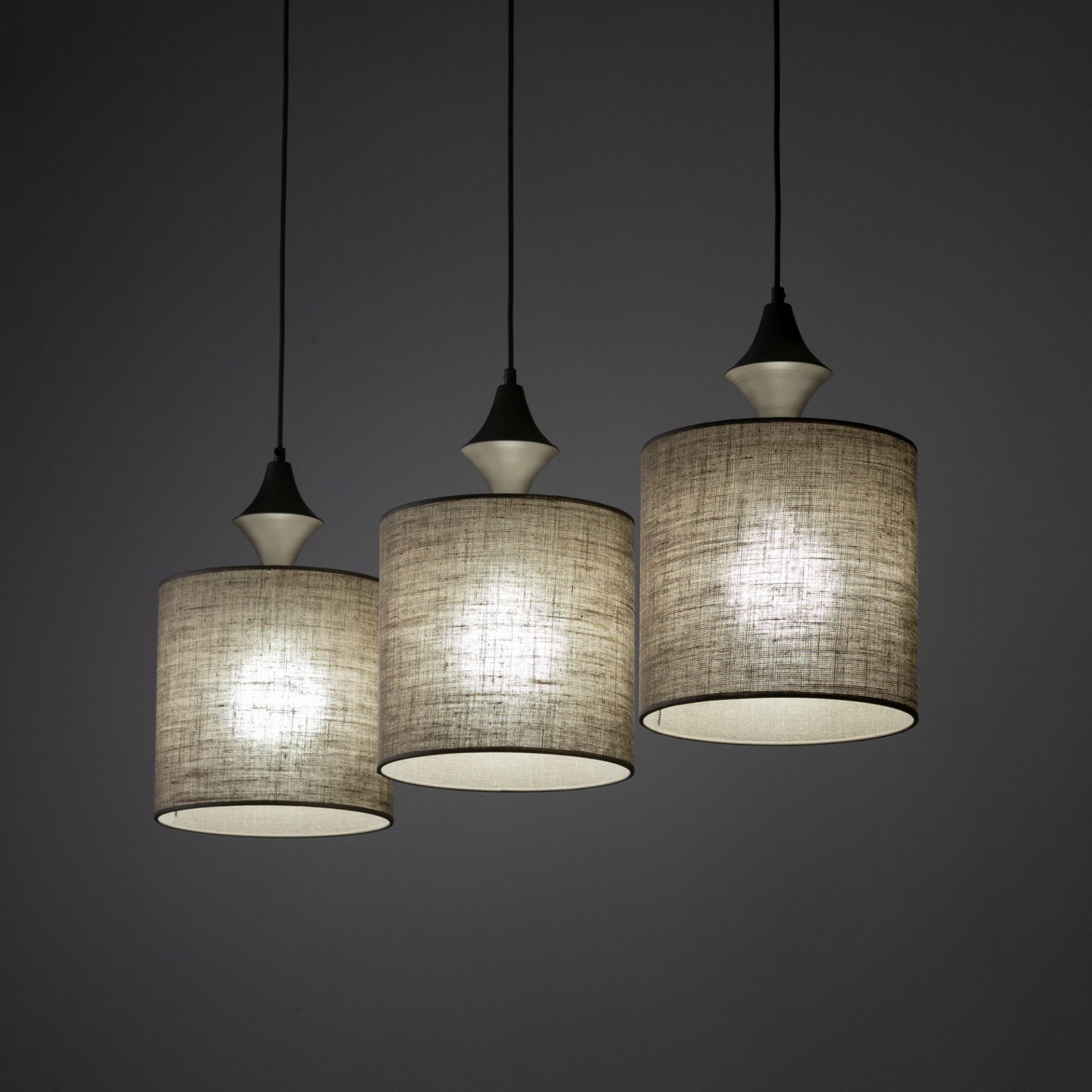 Trzy wiszące lampy z cylindrycznymi abażurami w kolorze brązowym, zawieszone na czarnych przewodach. Każda lampa ma stożkowy element dekoracyjny nad abażurem.