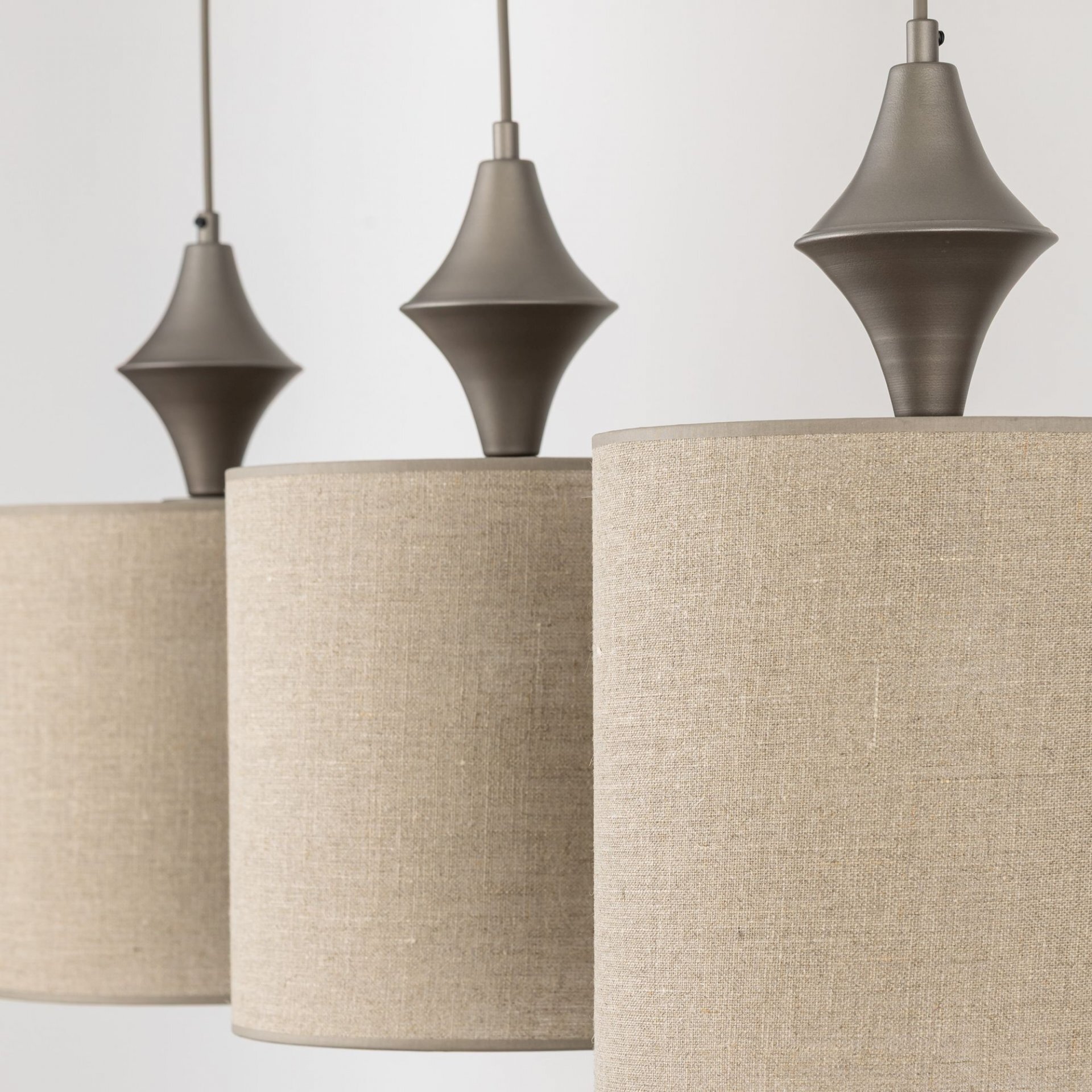 Trzy wiszące lampy z beżowymi, materiałowymi abażurami i metalowymi elementami w kolorze brązowym. Lampy mają nowoczesny design z regulowaną wysokością.