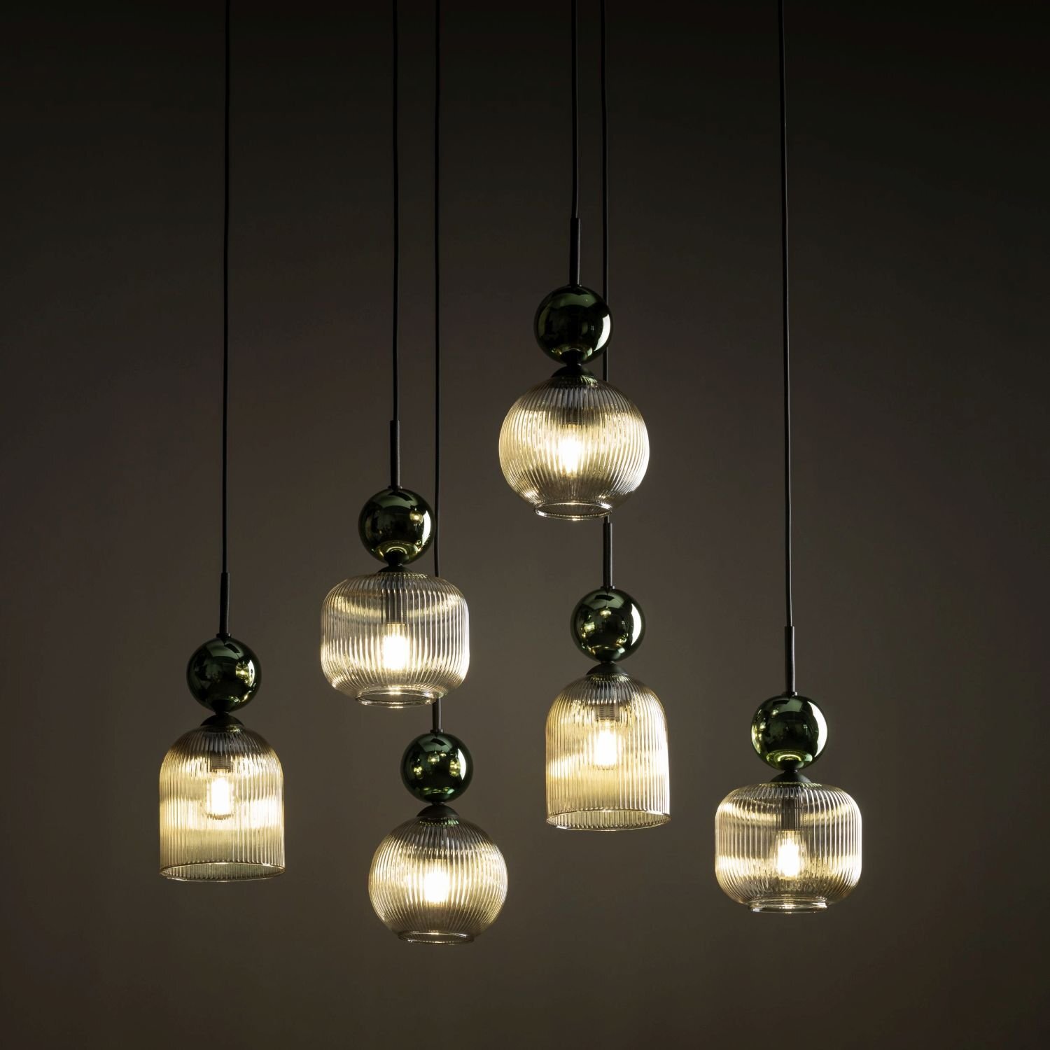 Zdjęcie przedstawia sześć wiszących lamp z przezroczystymi kloszami i ciemnymi elementami dekoracyjnymi. Lampy emitują ciepłe światło, a ich wysokość jest regulowana.