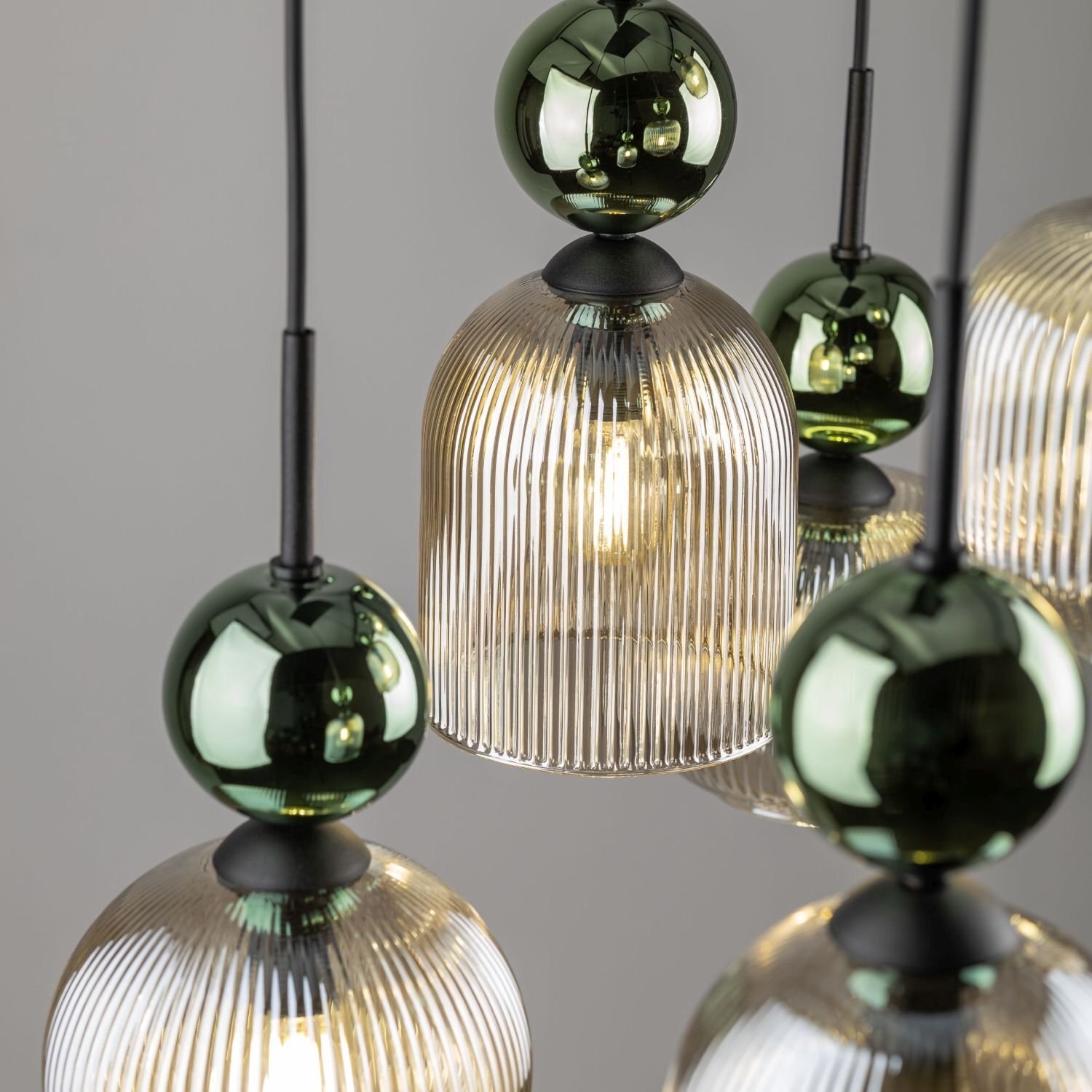 Zdjęcie przedstawia zbliżenie na lampę wiszącą z przezroczystymi, żebrowanymi kloszami i zielonymi, błyszczącymi kulami. Lampa ma nowoczesny design i jest wykonana z metalu oraz szkła.
