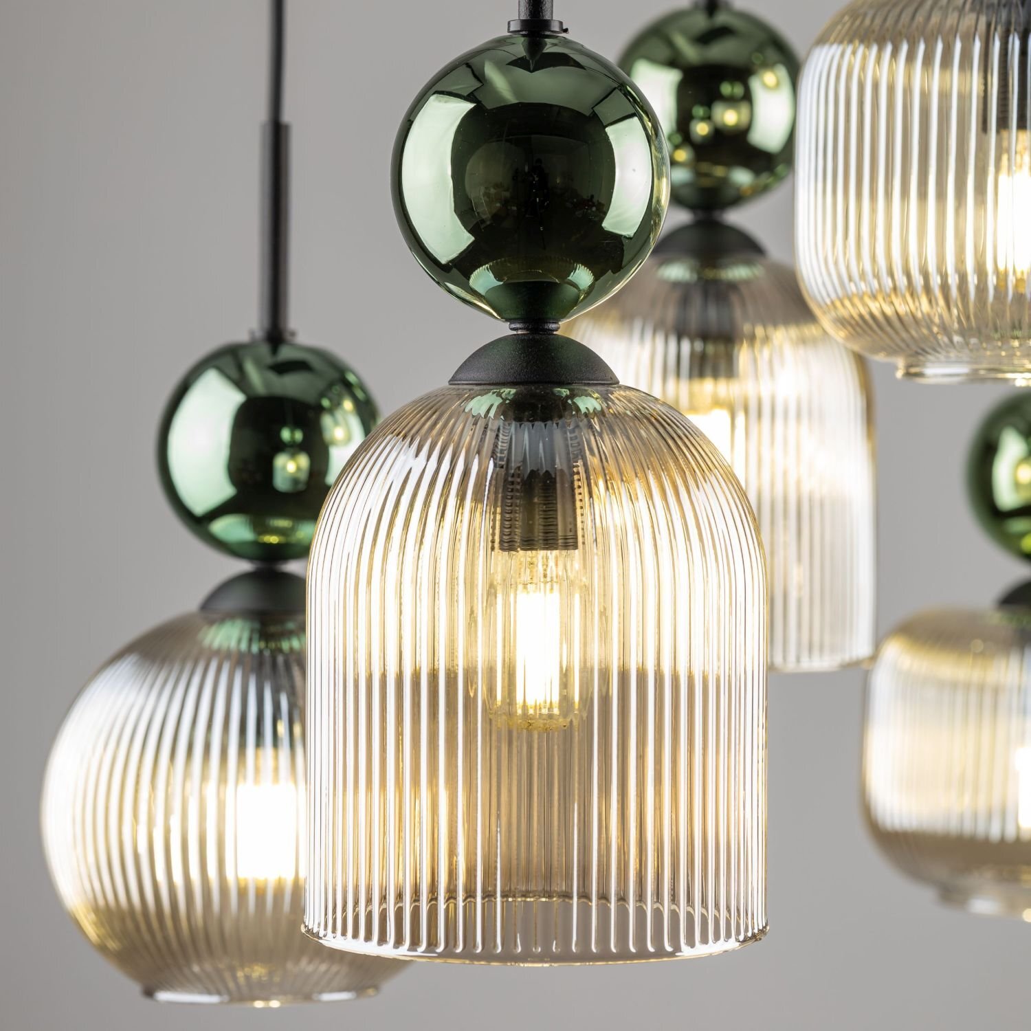 Zdjęcie przedstawia zbliżenie na kilka wiszących lamp z żarówkami, które mają szklane, żłobione klosze i zielone, kuliste elementy dekoracyjne. Światło żarówek jest ciepłe i rozproszone przez klosze.