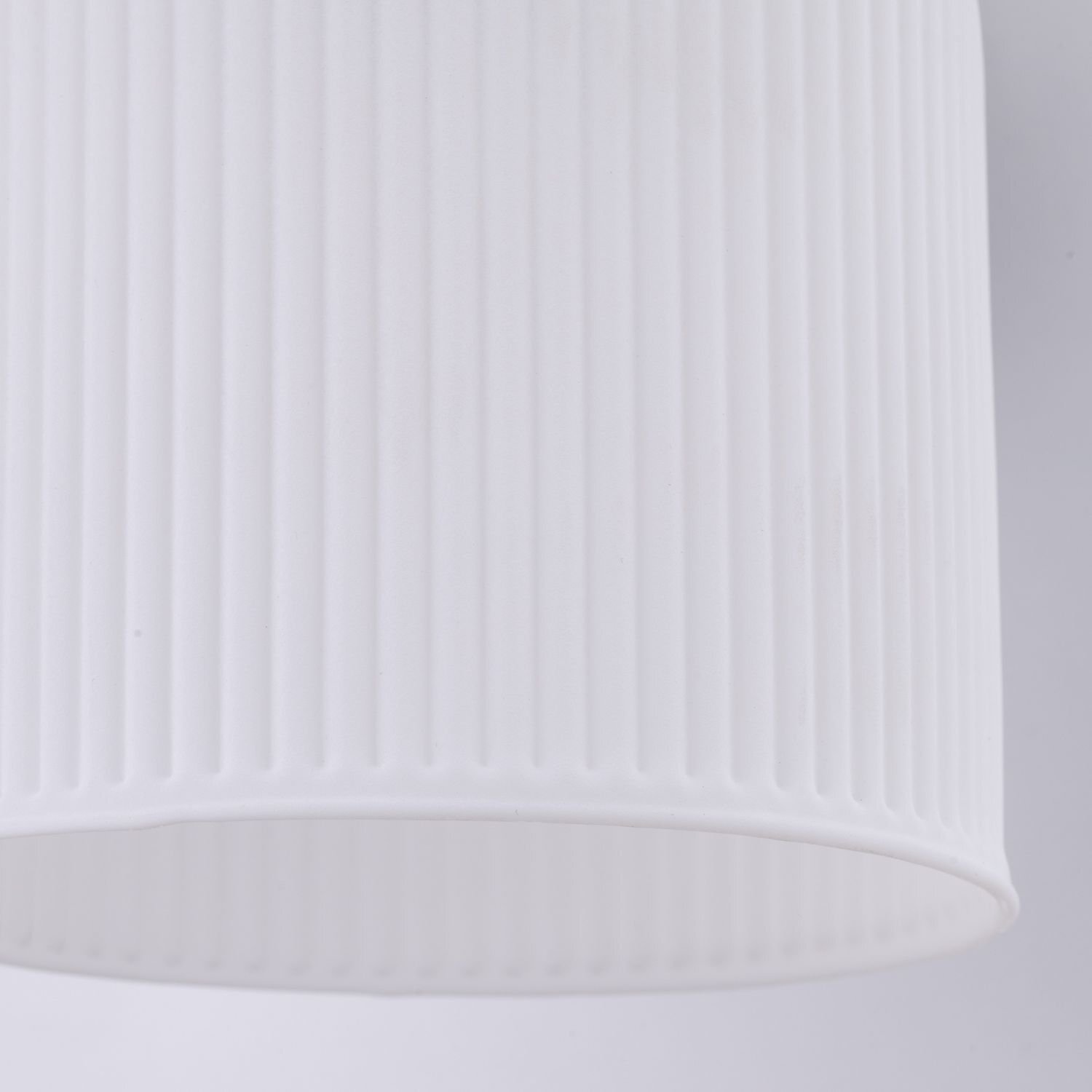 Biały, cylindryczny klosz z pionowymi żłobieniami. Materiał wygląda na szklany lub ceramiczny.