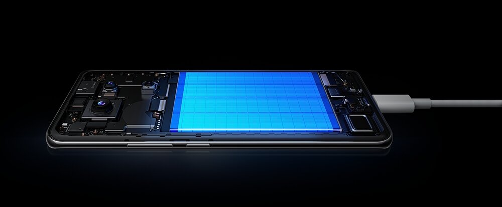 Obraz przedstawia smartfon z widocznym wnętrzem, podłączony do ładowarki. Ekran urządzenia jest podświetlony na niebiesko, ukazując wewnętrzne komponenty.