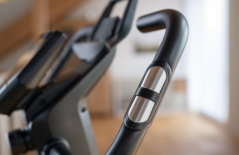 Zbliżenie na uchwyt roweru magnetycznego z metalowymi elementami. W tle widoczny jest wyświetlacz urządzenia.