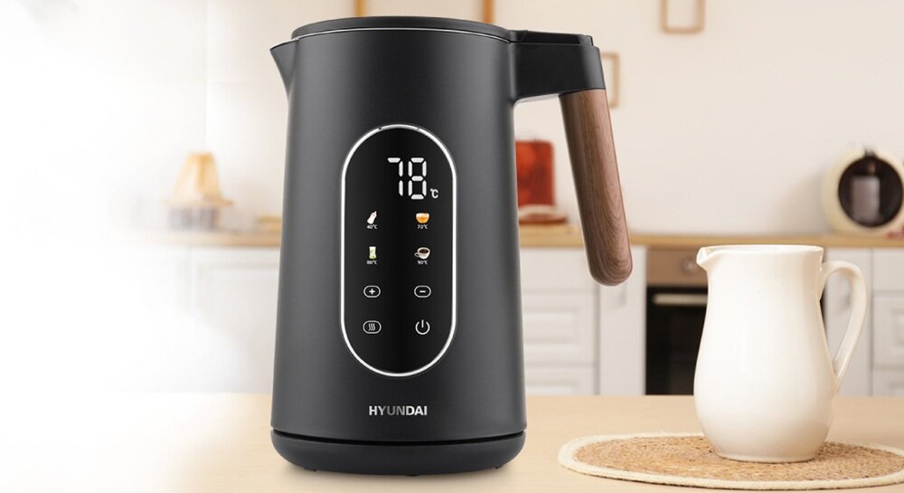 Czarny czajnik elektryczny z wyświetlaczem pokazującym temperaturę 78°C i ikonami funkcji. Obok czajnika stoi biały dzbanek na blacie kuchennym.