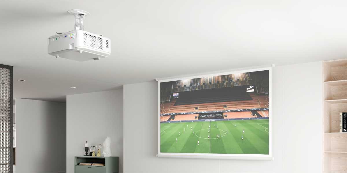 Uchwyt sufitowy HAMA 220879 Maksymalne obciążenie 13.5 kg Biały projektor zamontowany na uchwycie sufitowym wyświetlający mecz piłki nożnej na ekranie w jasnym salonie. 