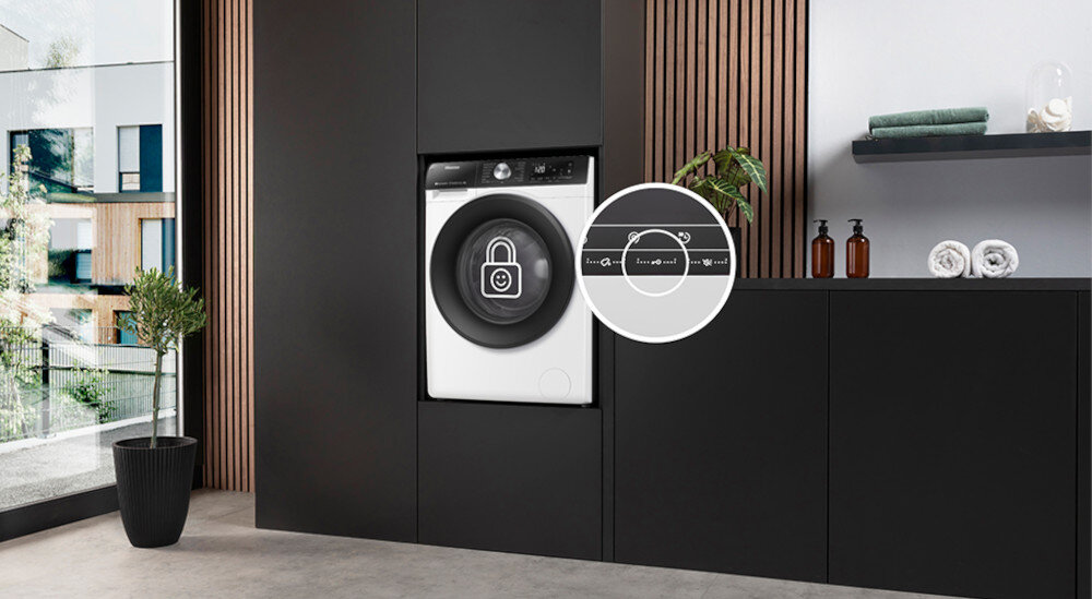 Pralka wbudowana w nowoczesną kuchnię z ciemnymi szafkami, obok której znajduje się powiększony widok panelu z ikoną kłódki. Na blacie stoją butelki i złożone ręczniki.