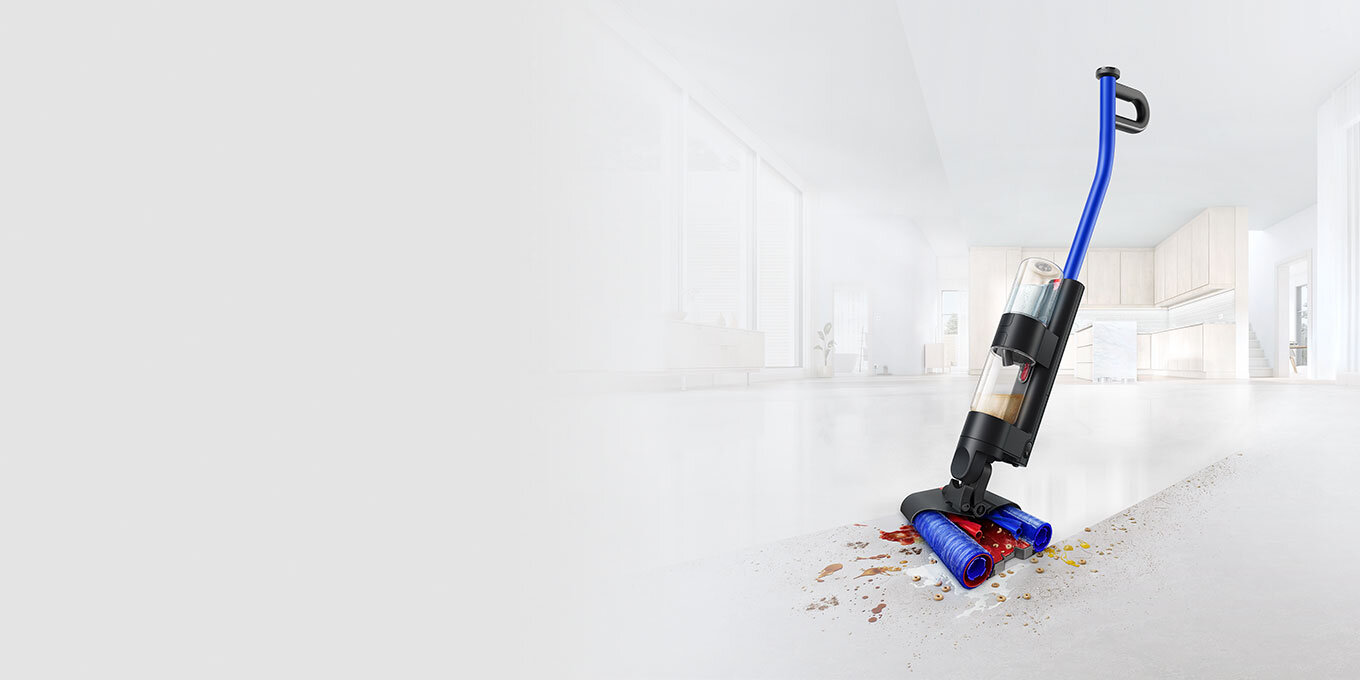 Na obrazie widoczny jest elektryczny mop z niebieską rączką, czyszczący podłogę z rozsypanych resztek. W tle znajduje się jasne, nowoczesne wnętrze kuchni.