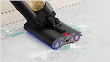 Na obrazie widać czarny mop elektryczny z dwoma okrągłymi szczotkami, czyszczący zabrudzoną podłogę. Podłoga jest pokryta plamami wody i brudu.