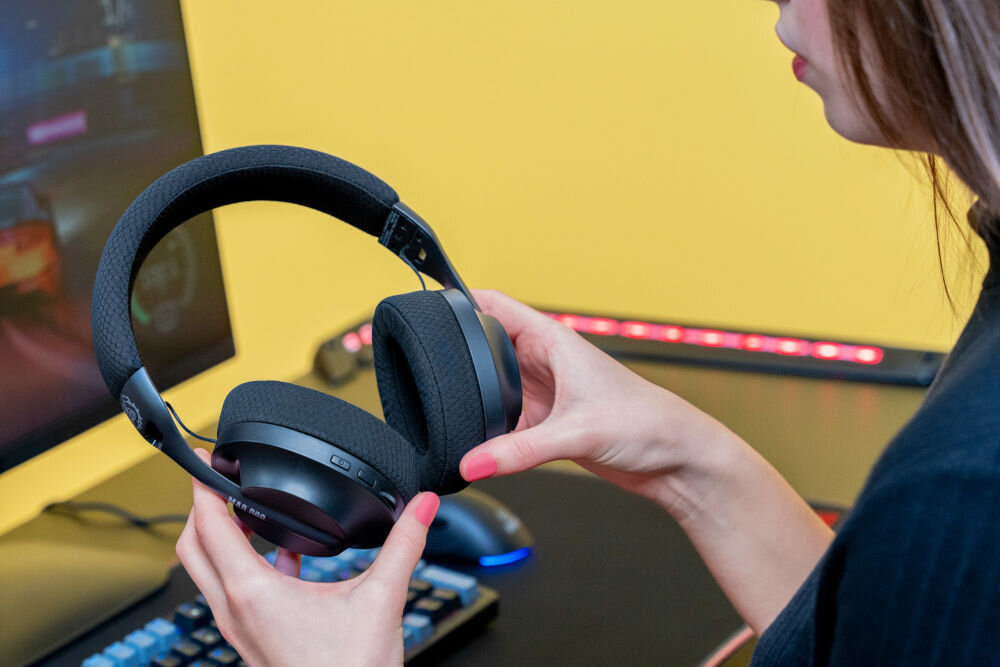 Słuchawki MAD DOG GH750K trzymane w rękach w tle komputer i podświetlana klawiatura