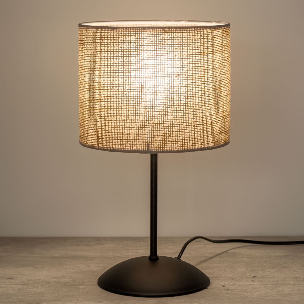 Lampka nocna z beżowym abażurem z juty na czarnej metalowej podstawie. Kabel zasilający widoczny obok podstawy.