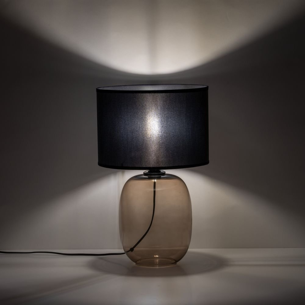 Na obrazie widoczna jest lampa stołowa z czarnym abażurem i szklanym kloszem w kolorze topazu. Lampa stoi na białej powierzchni, a światło tworzy wzór na ścianie.