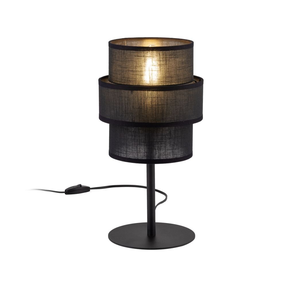 Czarna lampa stołowa z cylindrycznym abażurem, umieszczona na prostym metalowym stojaku z okrągłą podstawą. Lampa jest włączona, co powoduje delikatne rozświetlenie abażuru.