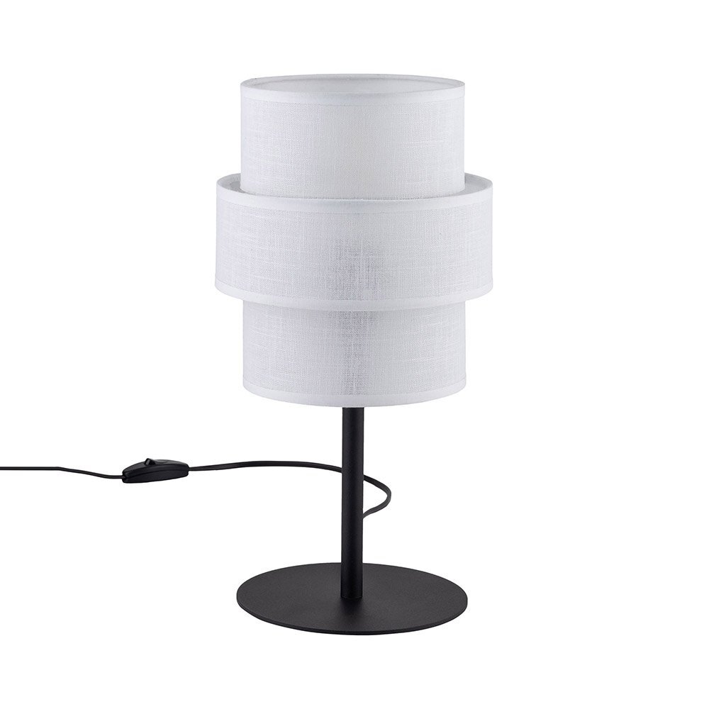 Na obrazie widoczna jest biała lampa stołowa z cylindrycznym abażurem, umieszczona na czarnej, metalowej podstawie. Obok lampy znajduje się czarny przewód z włącznikiem.