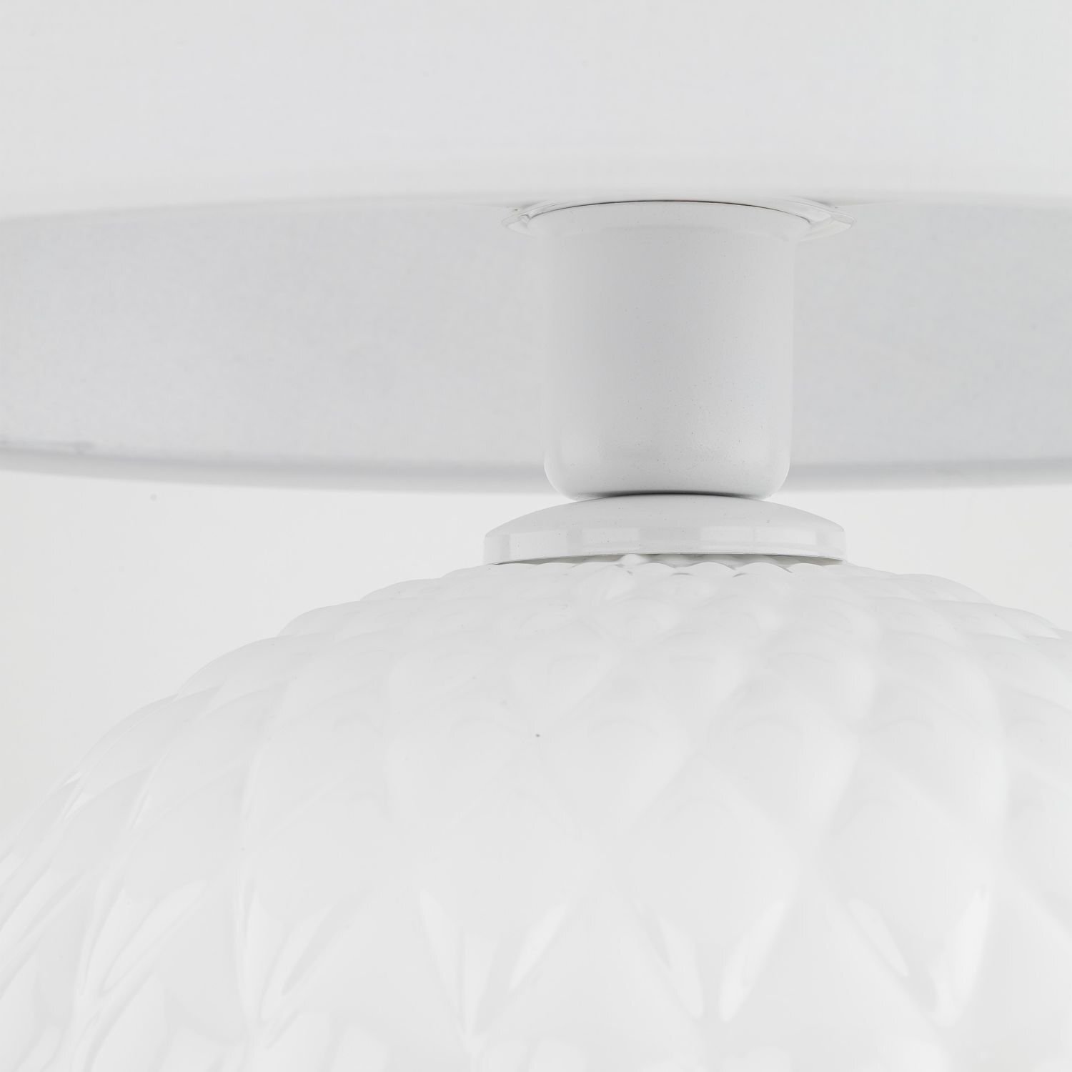 Zbliżenie na białą lampę stołową z teksturowaną podstawą i gładkim abażurem. Lampa wykonana jest z materiałów przypominających tkaninę i szkło.