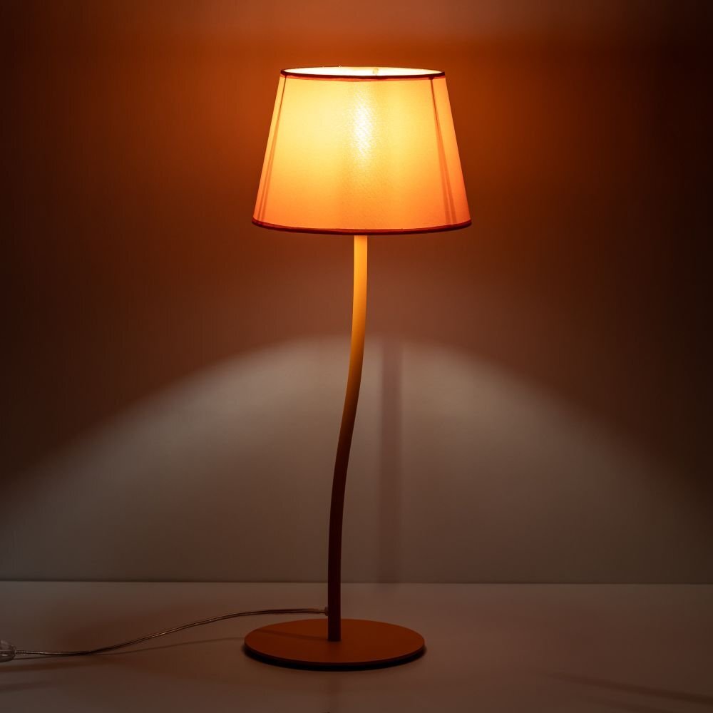 Na obrazie widoczna jest lampa stołowa z pomarańczowym kloszem, stojąca na płaskiej powierzchni. Lampa emituje ciepłe światło, tworząc przytulną atmosferę.