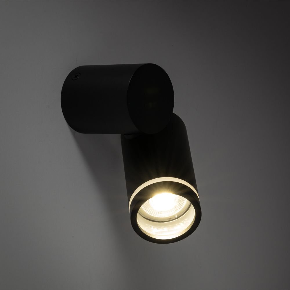 Czarny reflektor spot zamontowany na ścianie, emitujący jasne światło. Lampa ma cylindryczny kształt i nowoczesny design.