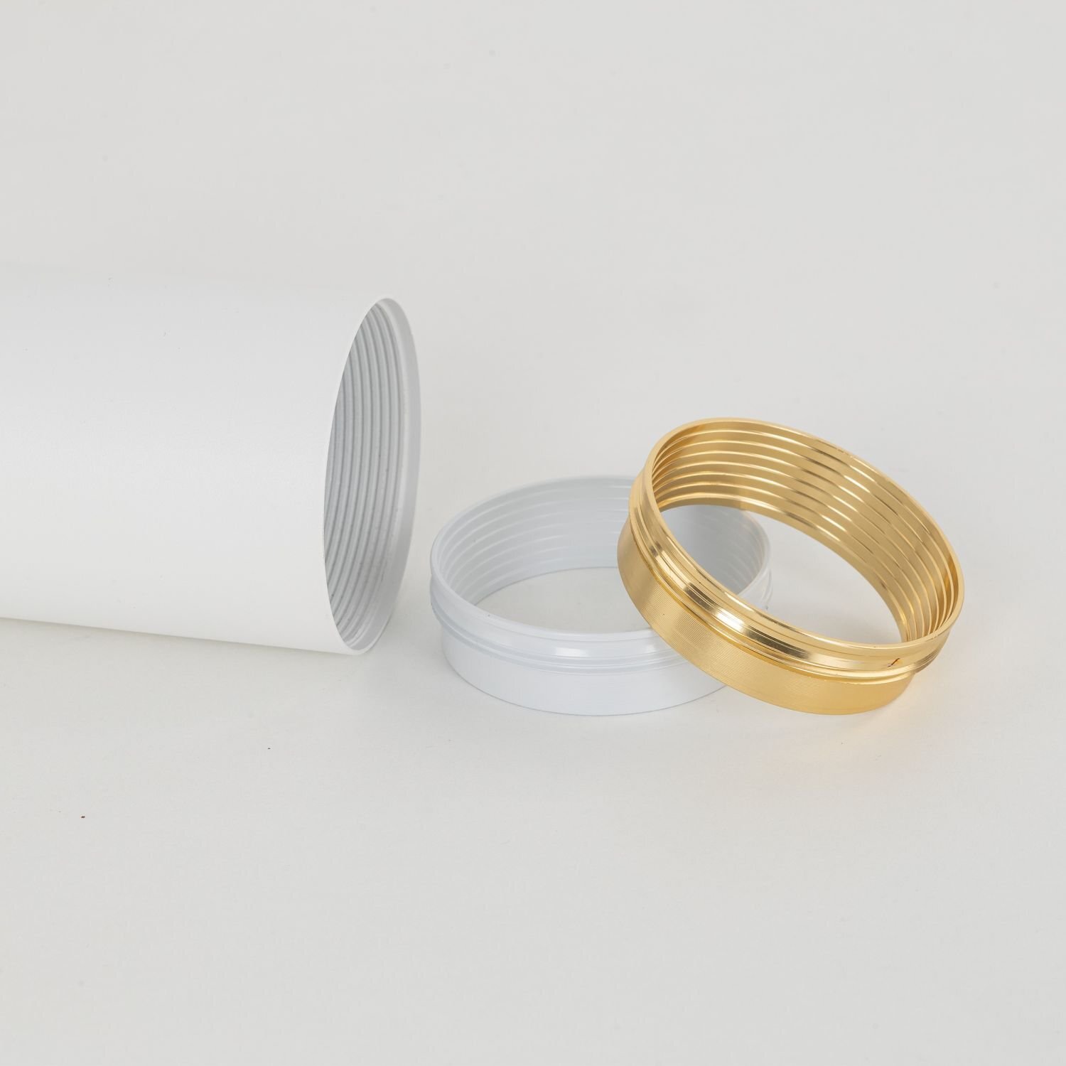 Na obrazie widoczny jest biały cylinder z gwintem oraz dwa pierścienie, jeden biały, drugi złoty. Elementy te są wykonane z metalu i mają nowoczesny design.