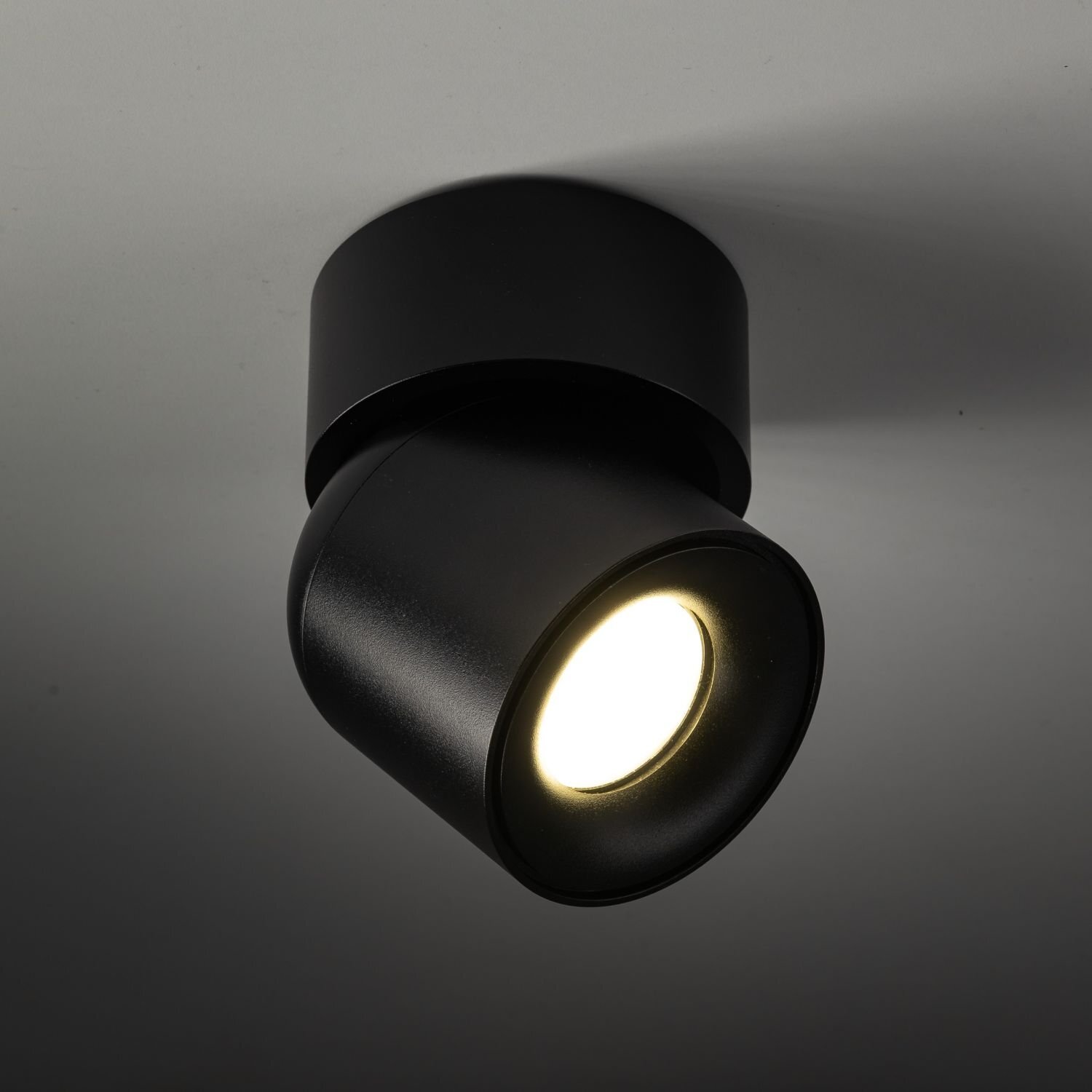 Czarny reflektor sufitowy z okrągłą podstawą i regulowanym kloszem, emitujący jasne światło. Produkt ma nowoczesny design i jest zamontowany na suficie.