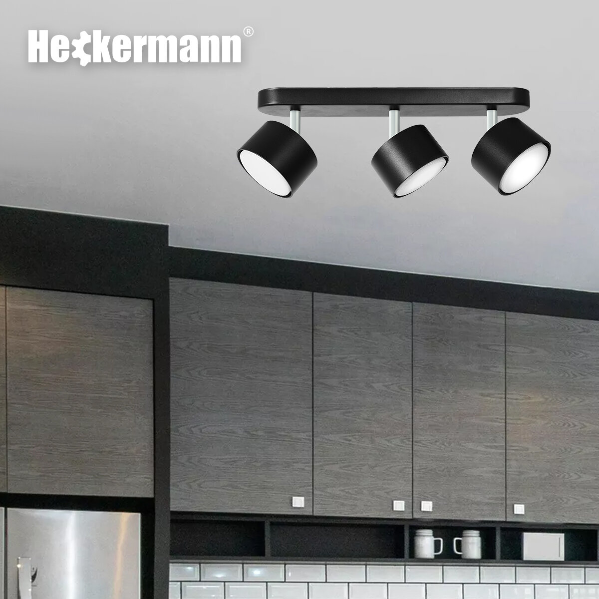 Czarna lampa punktowa LED z trzema głowicami zamontowana na suficie. W tle widoczne są szafki kuchenne, a w lewym górnym rogu znajduje się logo \'Heckermann\'.