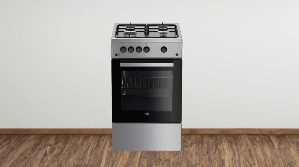 Na obrazie znajduje się wolnostojąca kuchenka gazowa z czterema palnikami i piekarnikiem. Kuchenka ma srebrny kolor z czarnym frontem piekarnika, a na drzwiach widoczne jest logo \'beko\'.