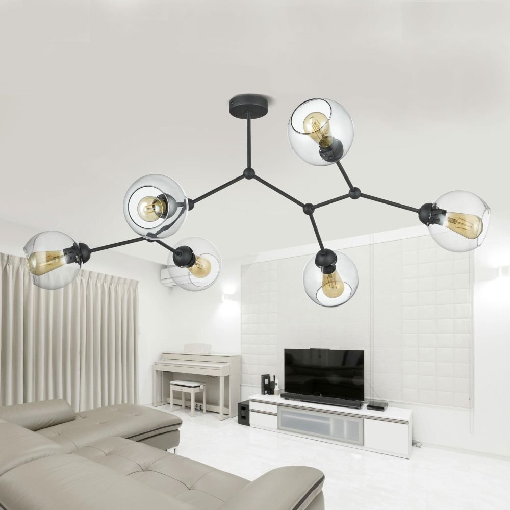Nowoczesna lampa sufitowa z sześcioma żarówkami w przezroczystych kloszach, zamontowana w jasnym, eleganckim salonie. W tle widoczna jest sofa, pianino oraz telewizor na szafce RTV.
