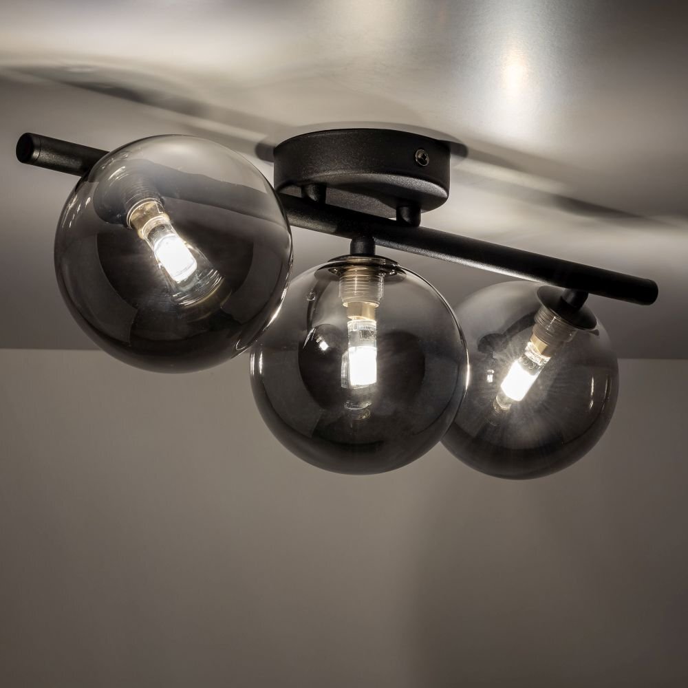 Czarna lampa sufitowa z trzema szklanymi kloszami w kształcie kul, zamontowana na metalowym uchwycie. Każdy klosz zawiera żarówkę emitującą jasne światło.