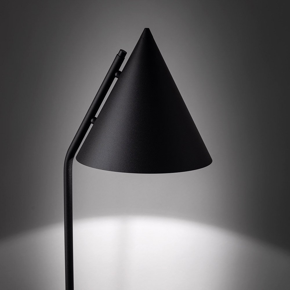 Czarna, metalowa lampa podłogowa o stożkowym kloszu, emitująca światło w dół. Tło jest szare, a lampa jest głównym elementem obrazu.