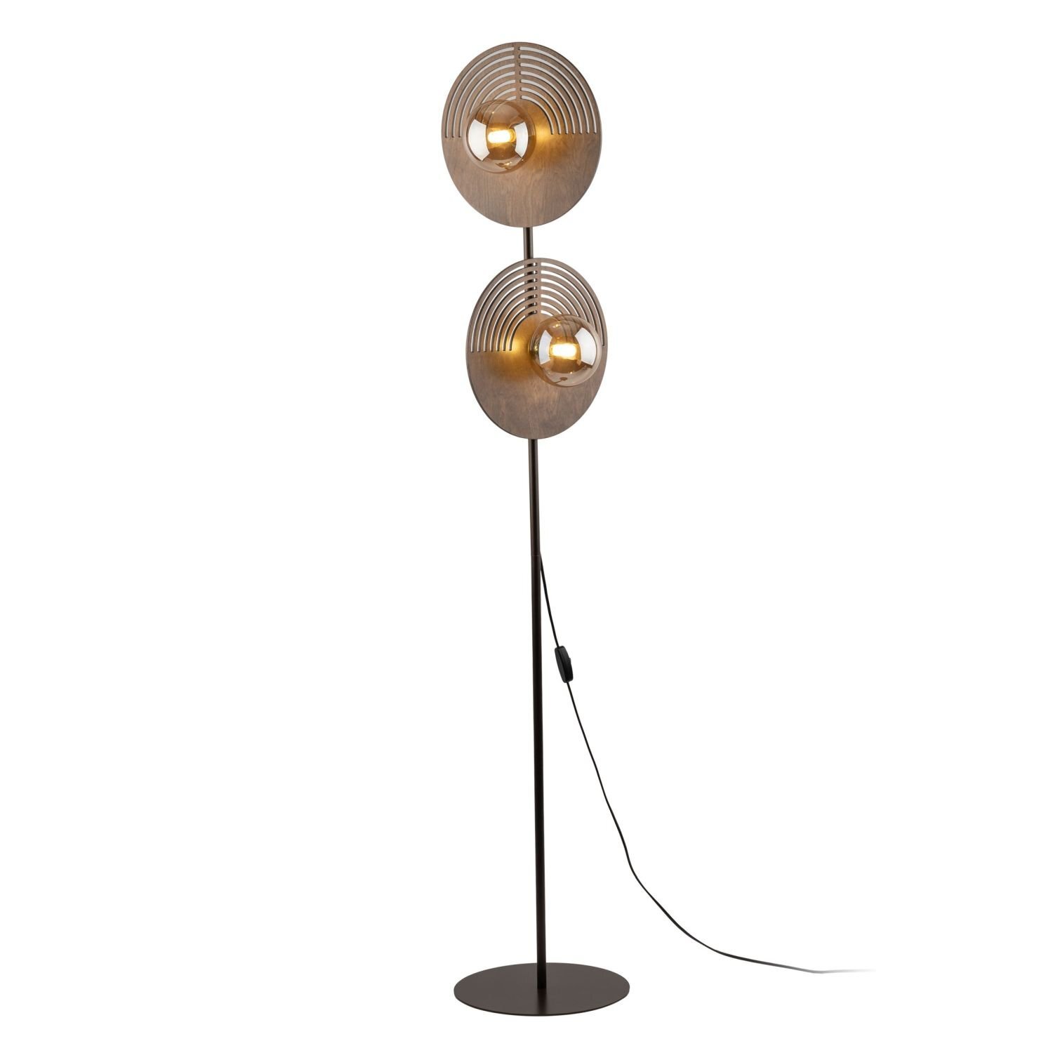 Lampa podłogowa z dwoma okrągłymi kloszami w kolorze dębu brązowego, zamontowana na smukłym, ciemnym stojaku z okrągłą podstawą. Klosze mają dekoracyjne, koncentryczne wzory i są wyposażone w żarówki, a z lampy wychodzi czarny przewód z włącznikiem.