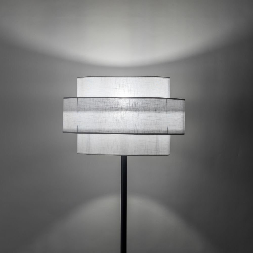 Lampa podłogowa z białym abażurem o nowoczesnym designie, umieszczona na czarnym stojaku. Światło tworzy delikatne cienie na ścianie.