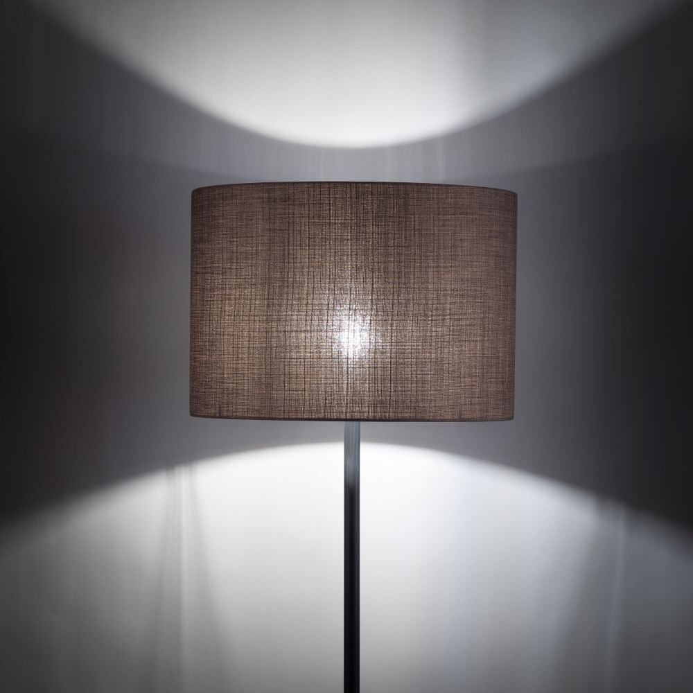 Lampa podłogowa z cylindrycznym abażurem w kolorze brązowym, emitująca rozproszone światło na ścianę. Podstawa lampy jest prosta i metalowa.