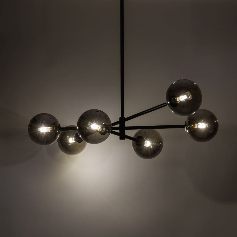 Na obrazie widoczna jest nowoczesna lampa sufitowa z sześcioma kulistymi kloszami w ciemnym kolorze, zamontowana na metalowej konstrukcji. Klosze emitują ciepłe światło, tworząc przytulną atmosferę.