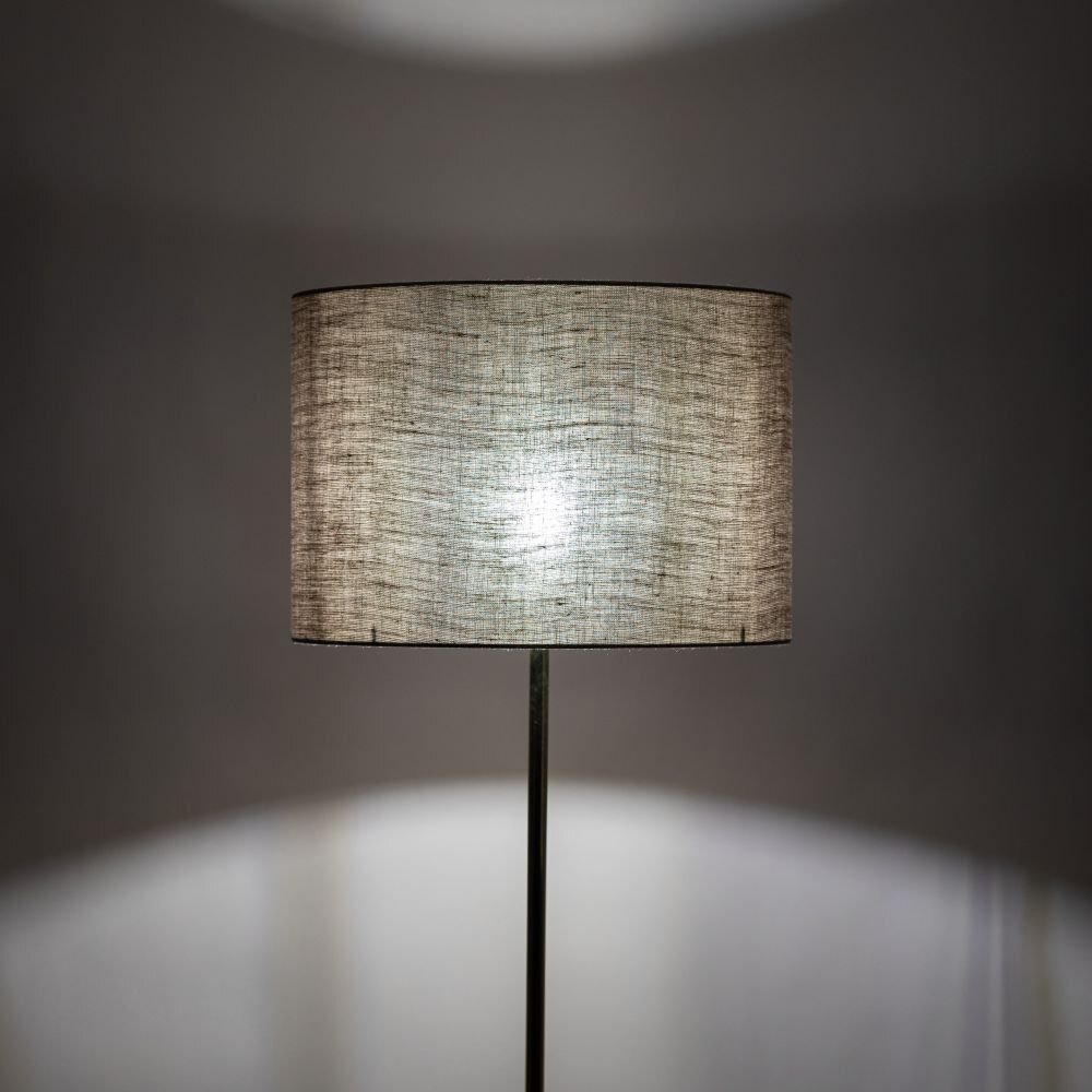 Lampa podłogowa z lnianym abażurem w kolorze złotym, emitująca miękkie światło. Tło jest jednolite i ciemne, co podkreśla jasność abażura.