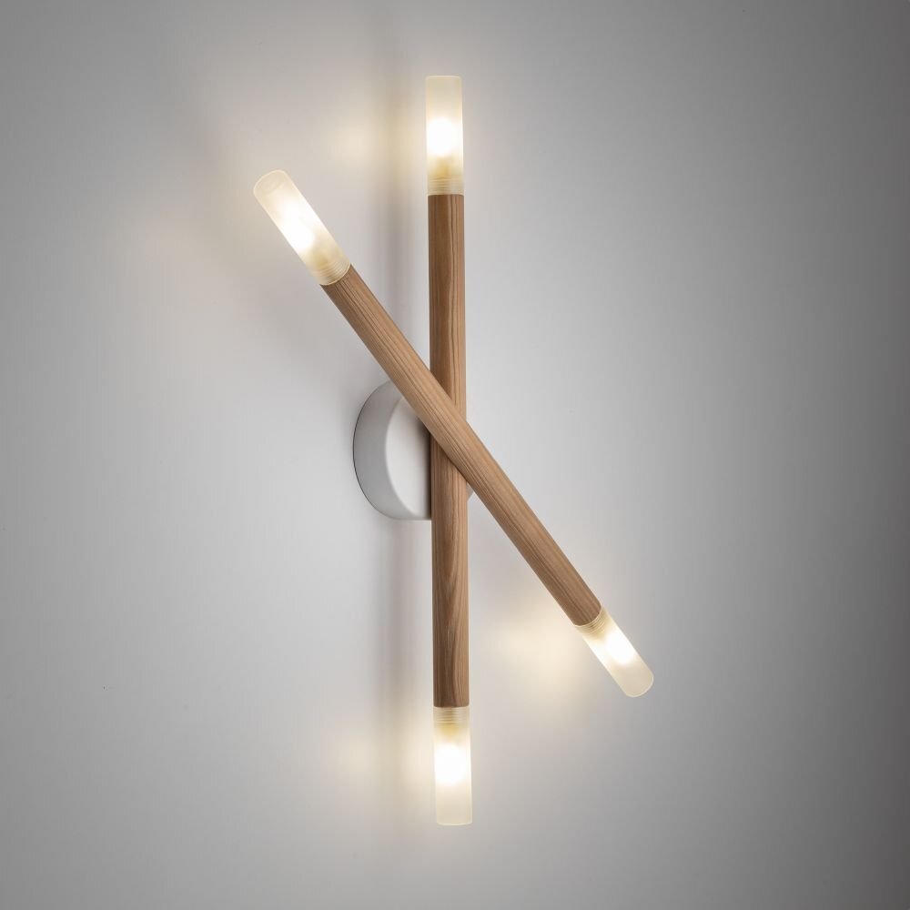 Na obrazie widoczna jest nowoczesna lampa ścienno-sufitowa z dwoma drewnianymi ramionami, zakończonymi szklanymi kloszami emitującymi światło. Lampa jest zamontowana na białej, okrągłej podstawie przymocowanej do ściany.