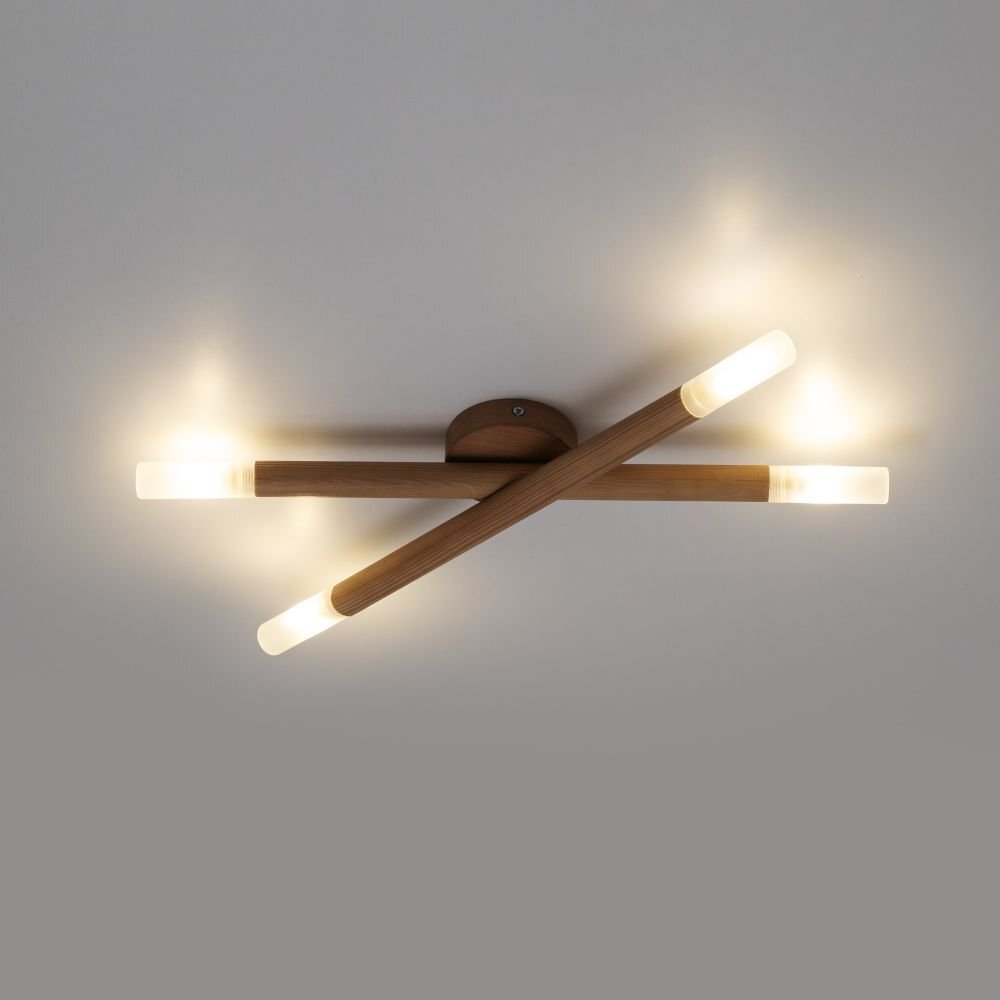 Na obrazie widoczna jest nowoczesna lampa ścienno-sufitowa z czterema źródłami światła, wykonana z drewna i białych elementów. Lampa emituje ciepłe światło, a jej konstrukcja składa się z dwóch skrzyżowanych ramion.