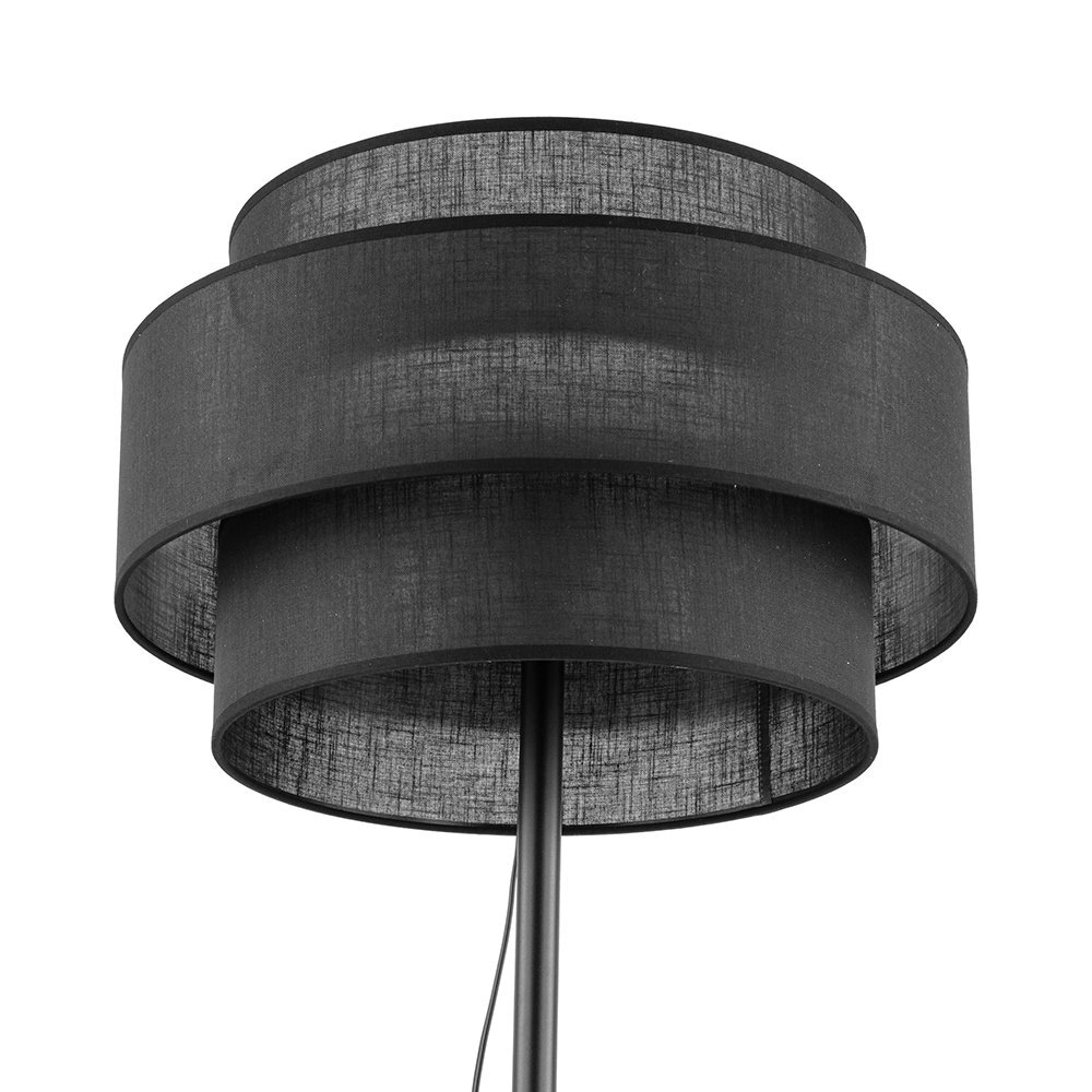Czarna lampa podłogowa z metalowym stelażem i abażurem w kształcie cylindrycznym. Abażur składa się z dwóch warstw materiału, tworząc nowoczesny design.