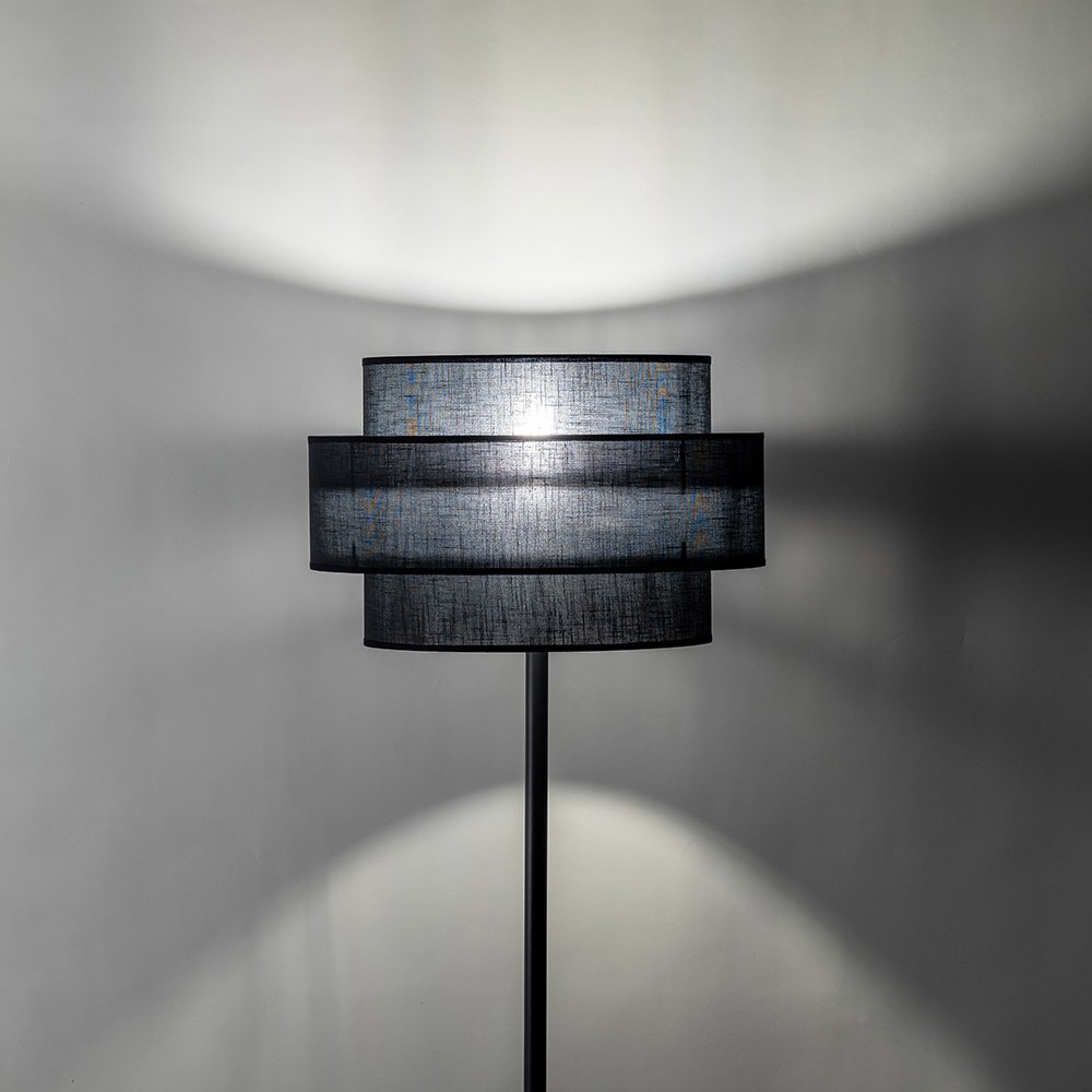 Czarna lampa podłogowa z metalowym stelażem i abażurem, emitująca światło na ścianę. Lampa ma nowoczesny design i jest przeznaczona do salonu lub sypialni.