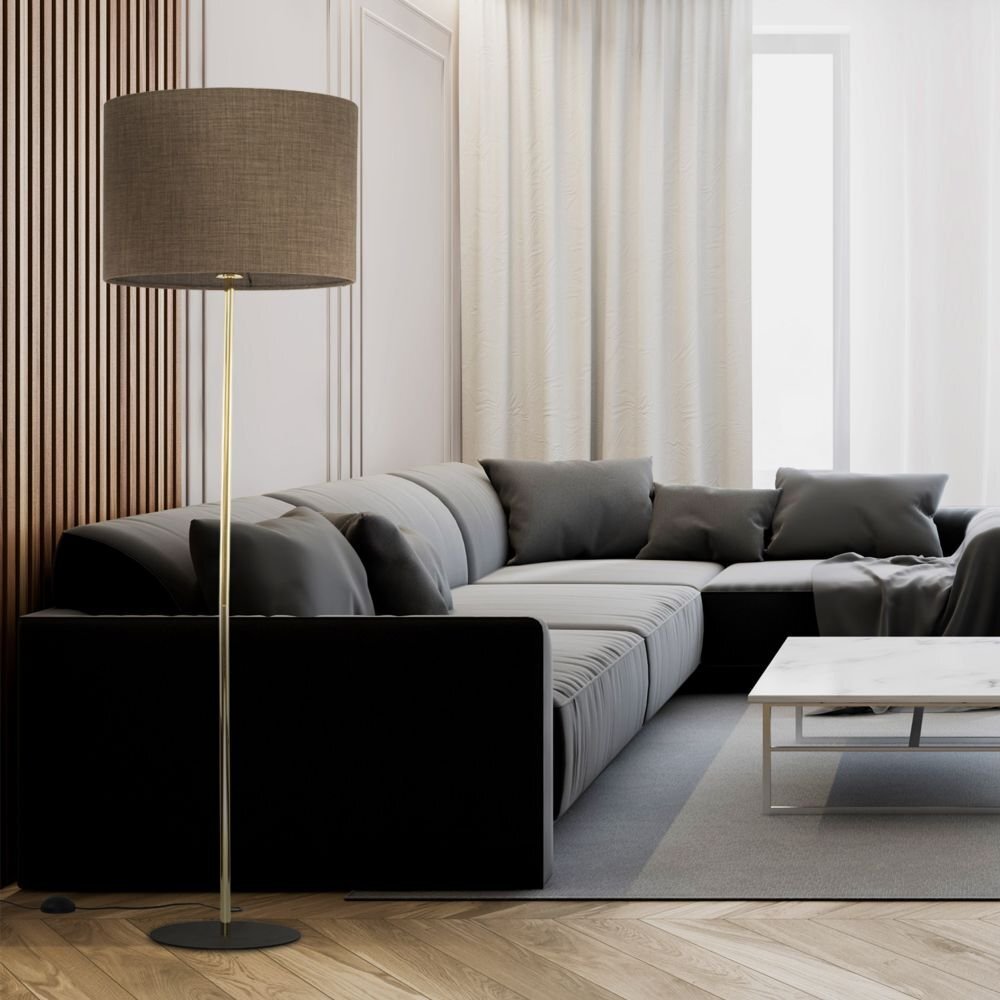 W nowoczesnym salonie znajduje się lampa podłogowa z brązowym abażurem i złotym stelażem. Obok lampy stoi duża, ciemna sofa z poduszkami oraz biały stolik na szarym dywanie.