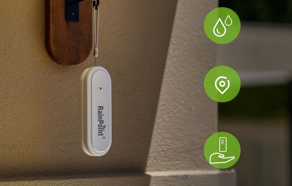 Inteligentny Termohigrometr RAINPOINT Smart+, monitoring, dane, aplikacja, kontrola, Biały czujnik RainPoint zawieszony na brązowym uchwycie przy ścianie, obok ikony kropel wody i lokalizacji.