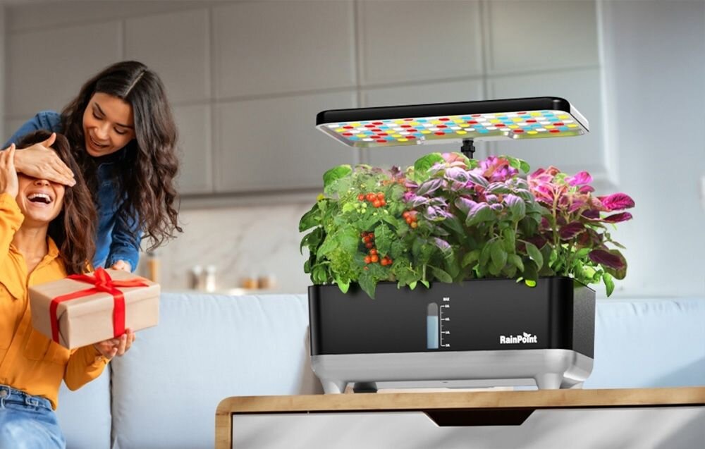 Na obrazie widoczna jest inteligentna doniczka z roślinami, nad którą znajduje się lampa LED. Na doniczce widnieje logo \'RainPoint\'.