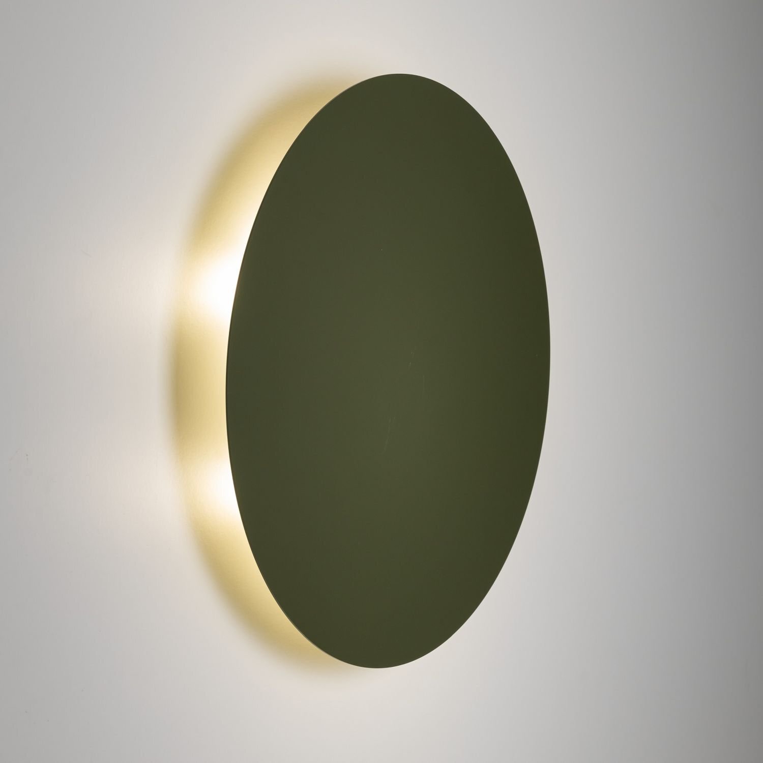 Okrągła, zielona lampa ścienna z metalu, emitująca delikatne światło wokół krawędzi. Lampa ma nowoczesny design i jest zamontowana na ścianie.