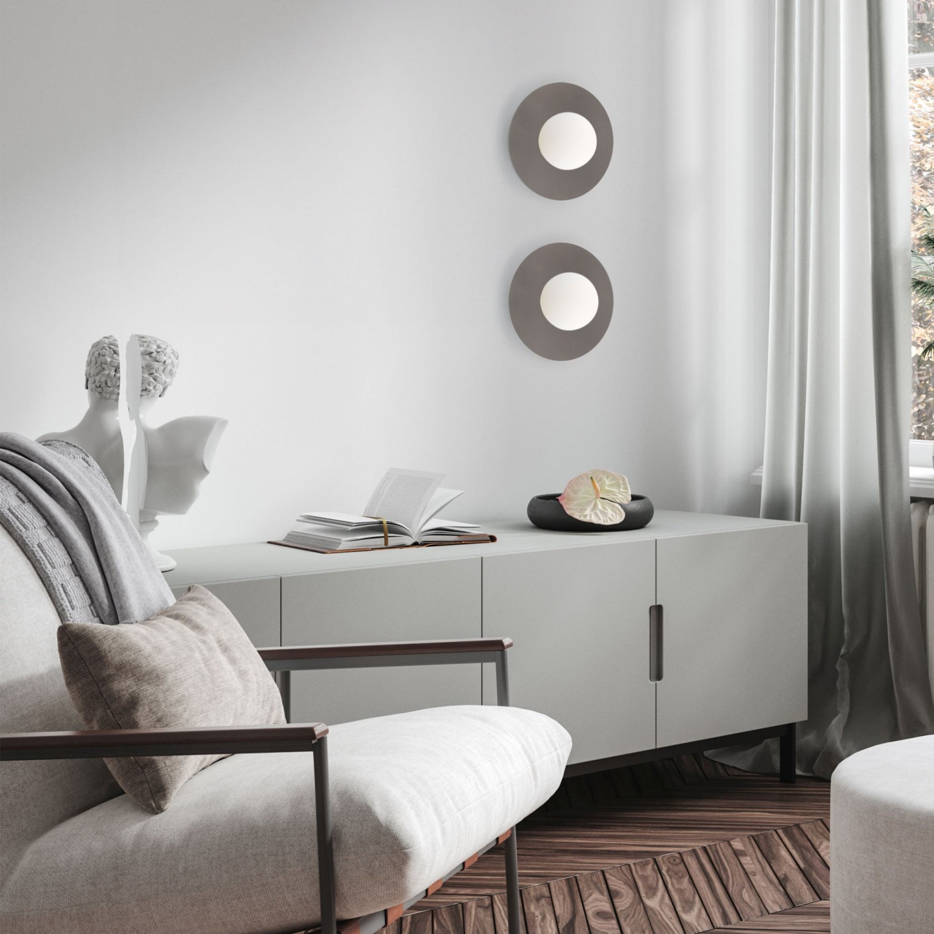Na ścianie znajdują się dwie okrągłe lampy o brązowych obwodach i białych środkach. W pomieszczeniu jest jasna sofa, szafka z książką i dekoracyjną rzeźbą oraz zasłony przy oknie.