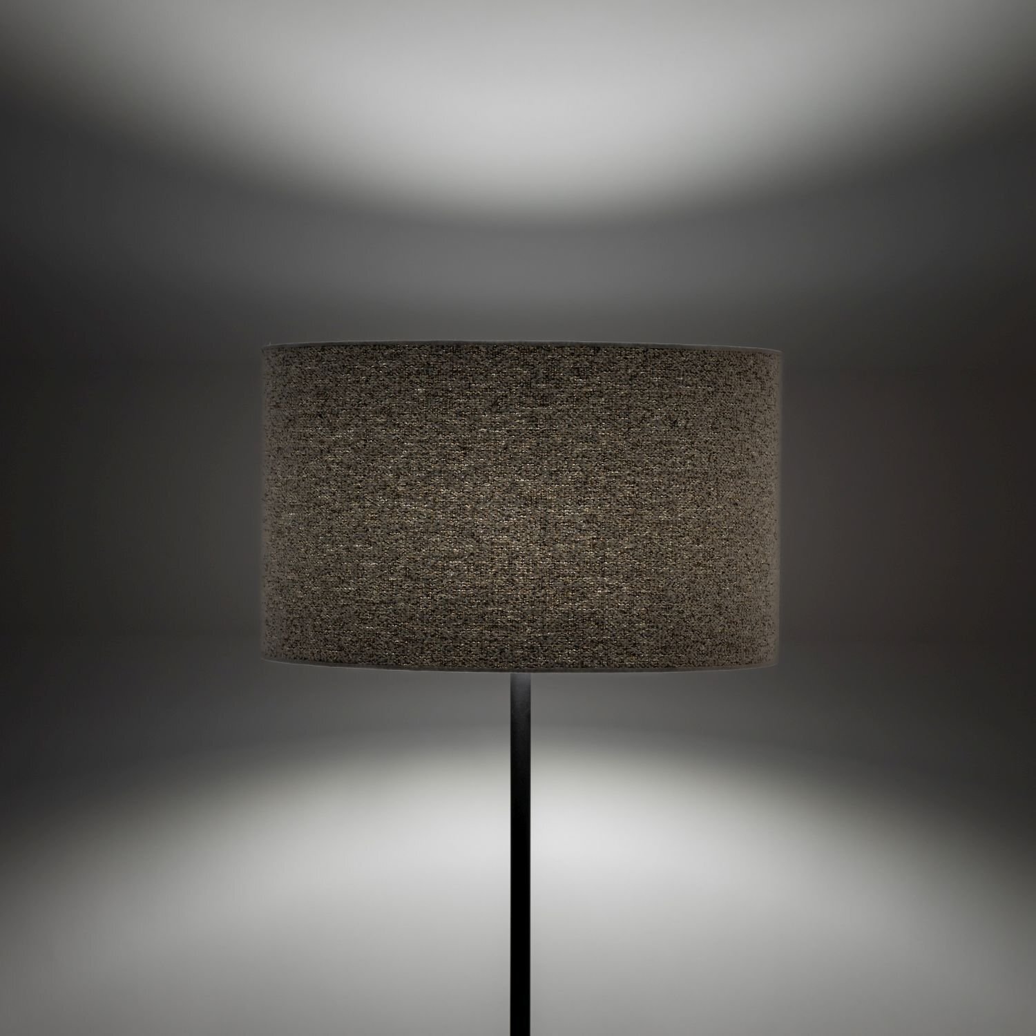 Na obrazie widoczna jest lampa podłogowa z ciemnym, cylindrycznym abażurem. Tło jest jednolite, a światło lampy tworzy delikatny efekt świetlny na ścianie.