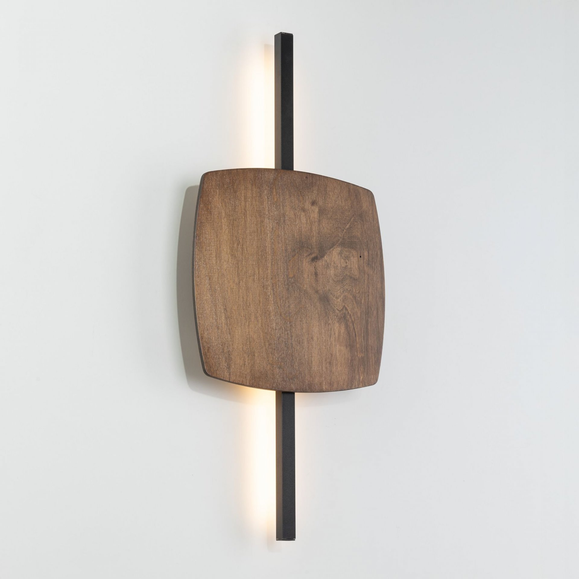 Kinkiet ścienny LED z drewnianym panelem i czarnym metalowym elementem, emitujący ciepłe światło. Lampa ma nowoczesny design i jest zamontowana na jasnej ścianie.