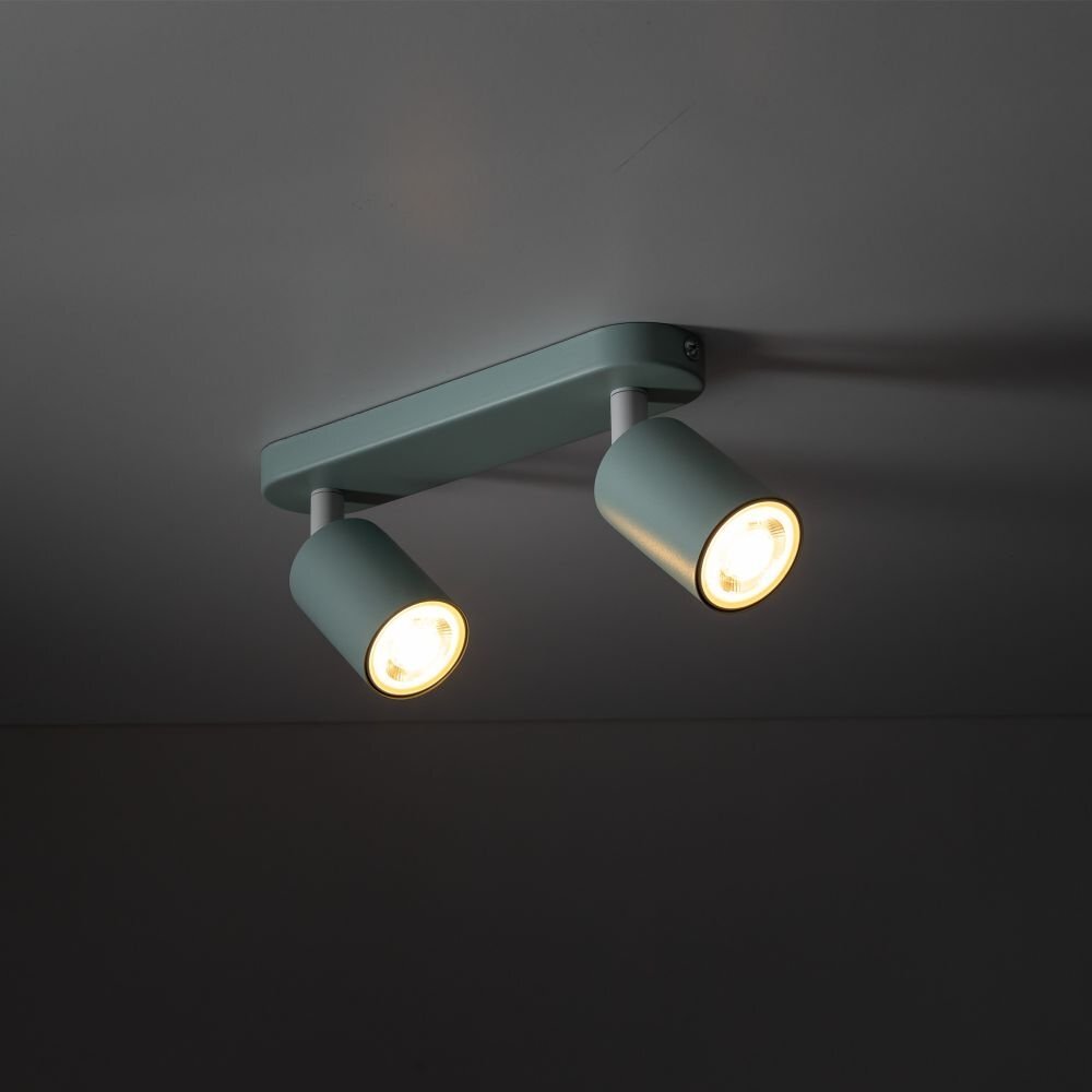 Na obrazie widoczna jest miętowa lampa sufitowa z dwoma regulowanymi reflektorami, zamontowana na ciemnym suficie. Reflektory emitują ciepłe światło.